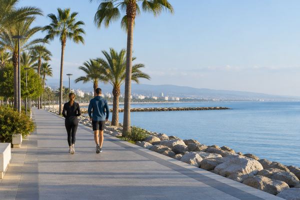Δύο άνθρωποι περπατούν γρήγορα σε παραλιακό πεζόδρομο με φοίνικες